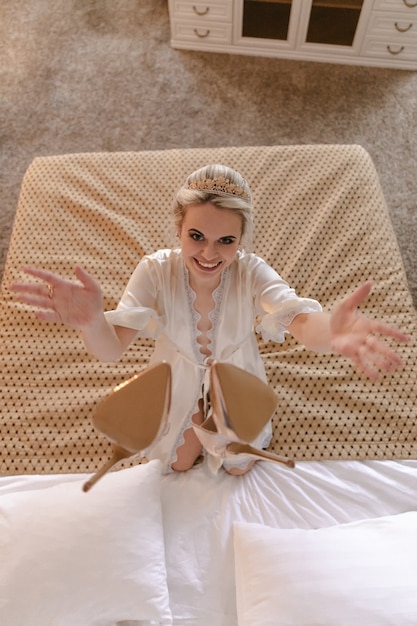 smiling blonde bride in a hotel room throws her shoes on the bed