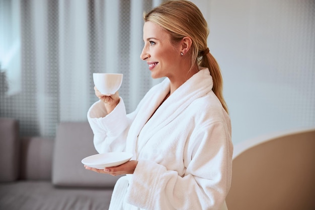 Smiling blonde female patient drinking a tisane