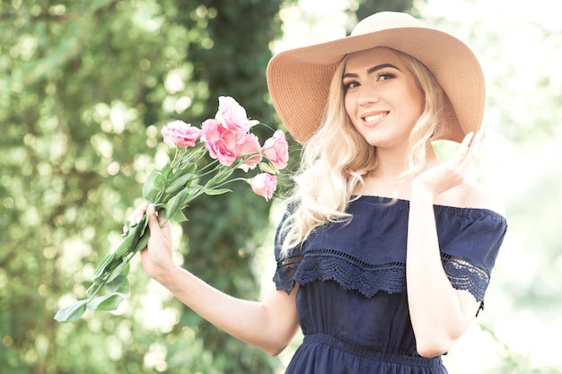 Smiling blonde girl holding flowers wearing straw hat outdoors Looking at camera Summer season