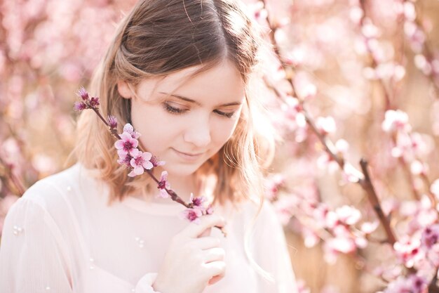 Smiling blonde girl holding peach flowers outdoors