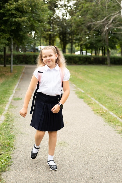 smiling blonde schoolgirl in school uniform with pink backpack going to school outdoor