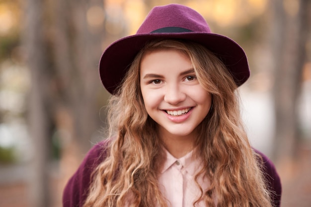 Smiling blonde teen girl wearing purple hat and jacket outdoors