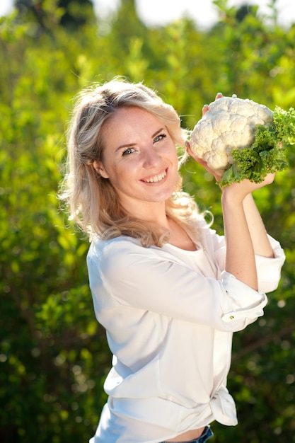 Smiling blonde woman hold fresh organic cauliflower over green nature background closeup. Healthcare