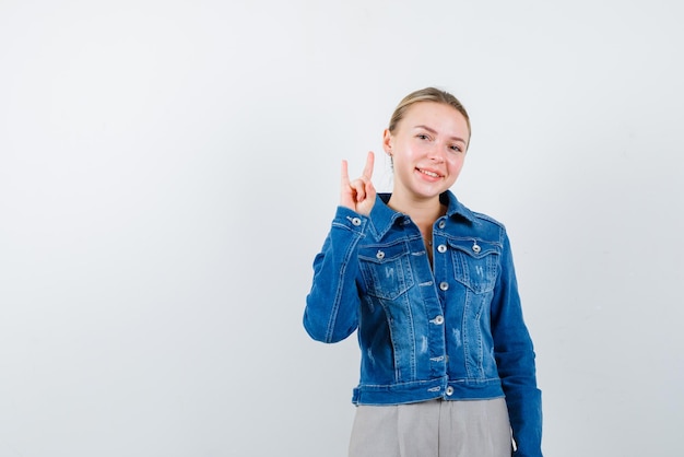 The smiling blonde woman is shoing victory gesture with hand on white background