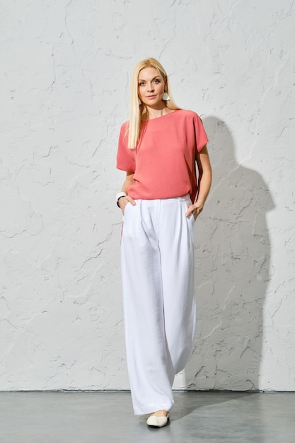 Smiling blonde woman in pink shirt and white trousers spring portrait