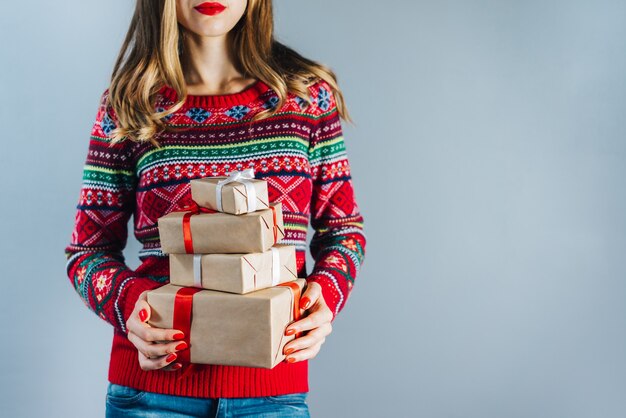 smiling blonde woman with red lips and polished nails holding bunch of gift boxes wrapped in craft paper and decorated with red satin ribbon. Christmas concept.