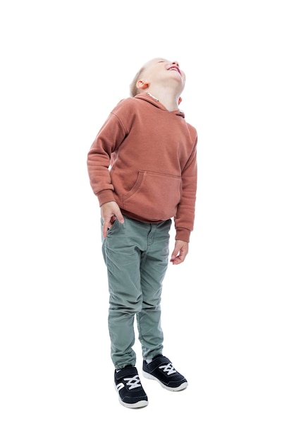 Smiling boy looks up A cute blonde in a brown hoodie and gray pants Full height Isolated on white background Vertical