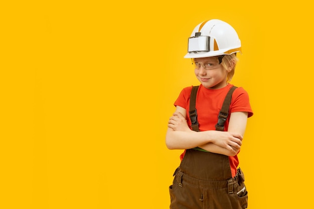 Smiling boy in protective helmet glasses and jumpsuit like worker Yellow background Copy space mock up