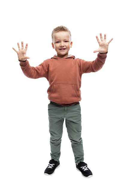 Smiling boy stands stretched out his hands, palms forward. A child in gray jeans and a brown jacket. Full height. Isolated on white background. Vertical.