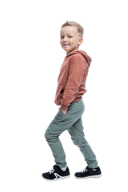 Smiling boy walking A cute blonde in a brown hoodie and gray pants Activity and positive Isolated on white background Full height Vertical Side view