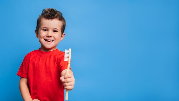 A smiling boy with healthy teeth holds a toothbrush on a blue isolated background Oral hygiene A place for your text