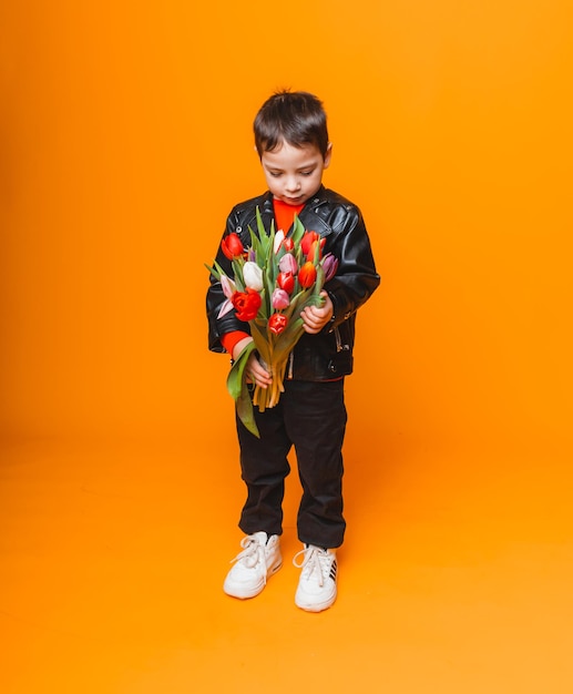 Smiling boy with spring flower bouquet of tulips isolated on yellow Little boy holding tulips