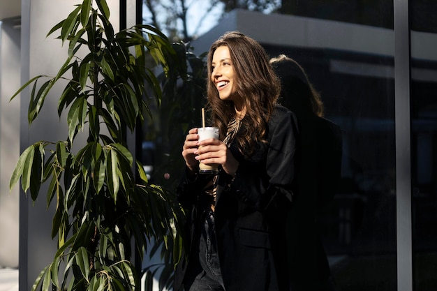 Smiling brunette girl drinks latte or cappuccino holds a cup in her hands Attractive young woman relaxing in a cafe