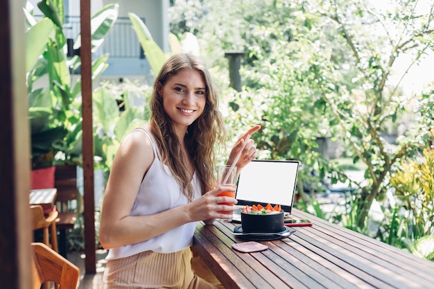 smiling brunette looking at camera and drinking juice on wooden table with bowled beverage