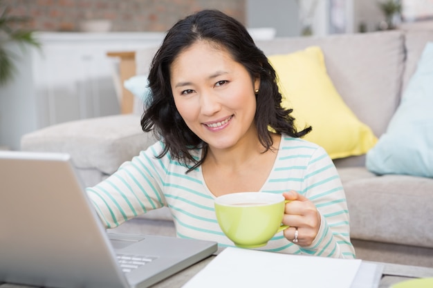 Smiling brunette using laptop and holding mug in the living room