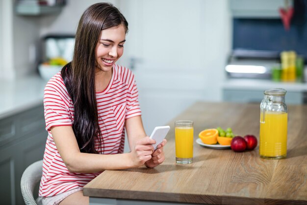 Smiling brunette using smartphone in the kitchen