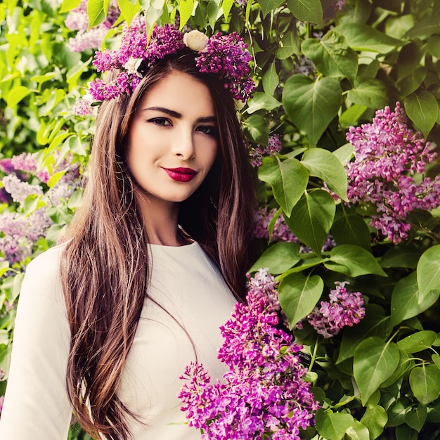 Smiling Brunette Woman Fashion Model with Long Healthy Hair Makeup and Flower Wreath on Floral Background