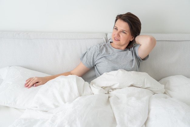 Smiling brunette woman wearing pajama sitting in bed in bedroom