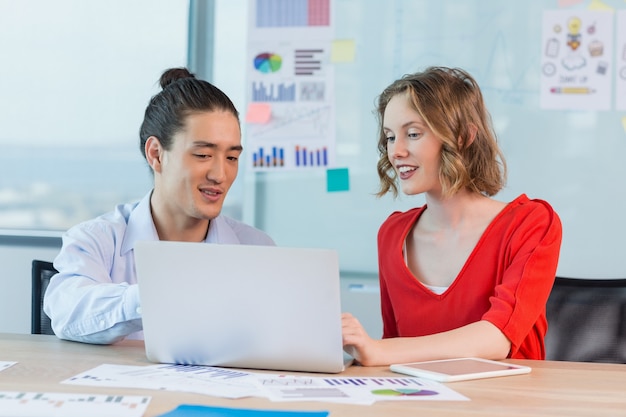 Smiling business colleagues discussing over laptop in conference room