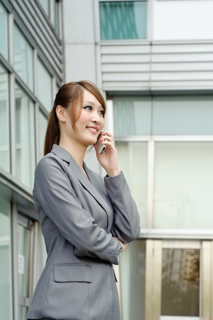 Smiling business manager woman using cellphone, half length closeup portrait outside of modern buildings.