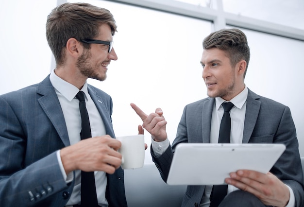 Smiling business partners interacting in the office during a coffee break and using a tablet