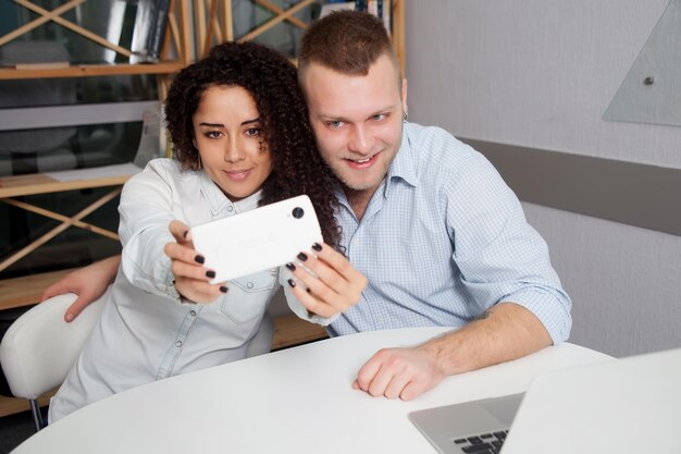 Smiling business people taking selfie on smartphone while sitting on desk in office