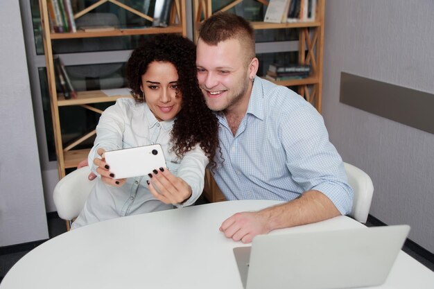 Smiling business people taking selfie on smartphone while sitting on desk in office