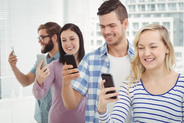 Smiling business people using smartphones while standing in row 