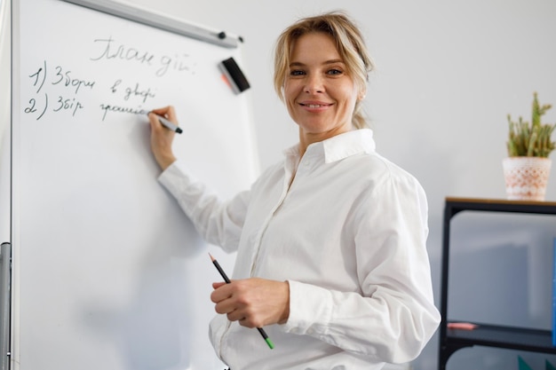 Smiling business woman in formal wear writes on flipchart during presentation or lecture in office