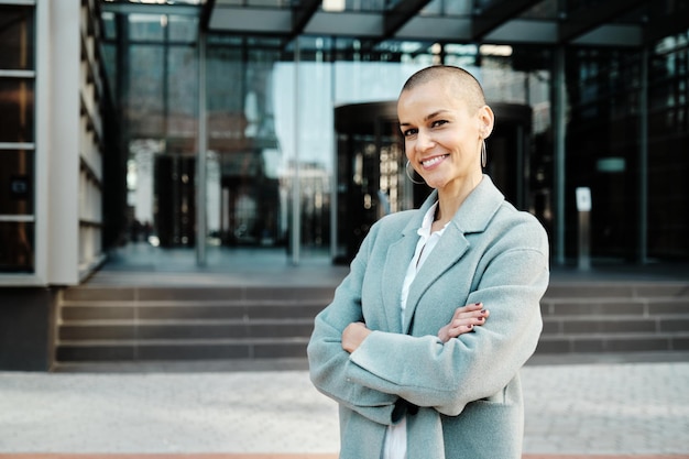 Smiling business woman posing with her arms crossed outside office buildings at financial district.