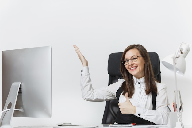 Smiling business woman sitting at the desk, working at computer with documents in light office