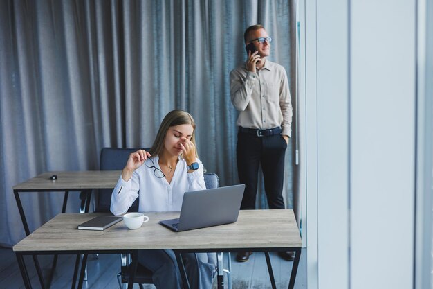 Smiling business woman sitting at a table with a laptop keeping her back to her partner sitting at the desktop The concept of successful teamwork