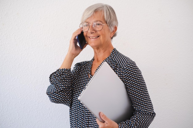 Smiling business woman talking on mobile phone isolated on white background Senior lady holding laptop under her arm