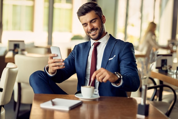 Smiling businessman enjoying in coffee break and using smart phone in a cafe