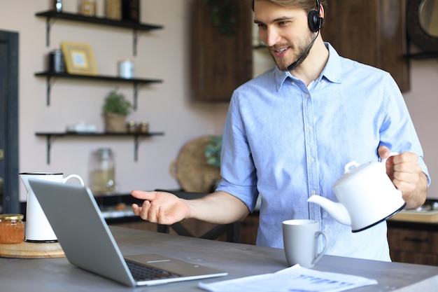 Smiling businessman greeting colleagues in video conference and negotiating distantly from home.