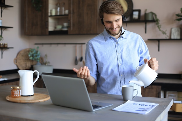 Smiling businessman greeting colleagues in video conference and negotiating distantly from home.