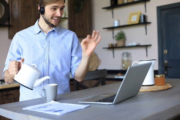 Smiling businessman greeting colleagues in video conference and negotiating distantly from home.