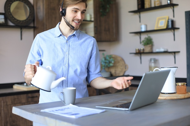 Smiling businessman greeting colleagues in video conference and negotiating distantly from home.