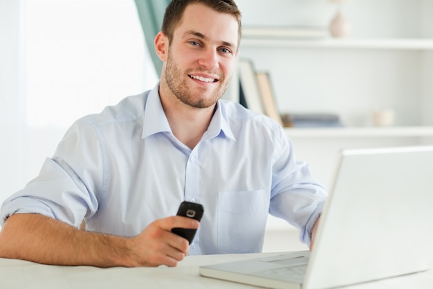 Smiling businessman holding his cell while typing on his laptop