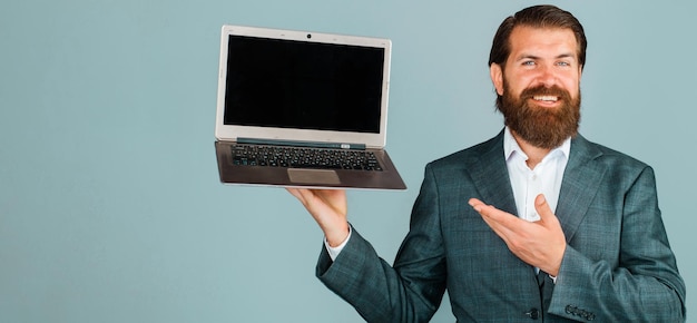 Smiling businessman shows with hand at laptop bearded man with computer blank screen on notebook