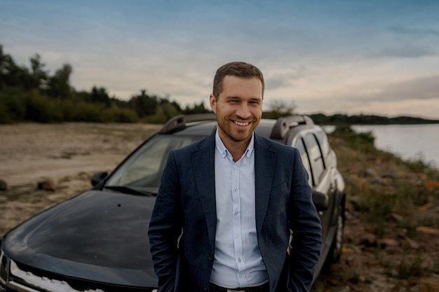 Smiling businessman with black classic car wearing suit. Successful man is standing near his car outdoors.