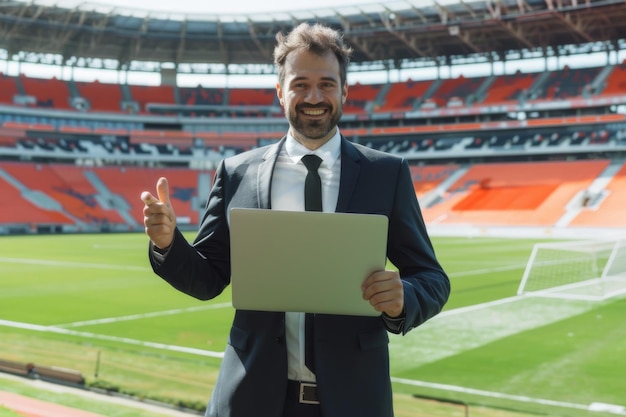 Photo smiling businessman with laptop giving thumbs up at a soccer stadium