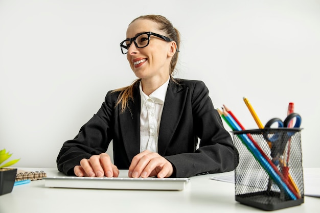 Smiling businesswoman in glasses typing on keyboard while sitting at workplace