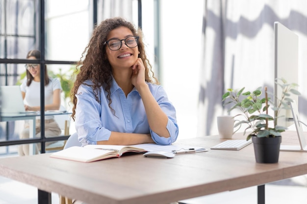 Smiling businesswoman looking at camera make conference or business call recording video blog talking with client Collegue is on the background