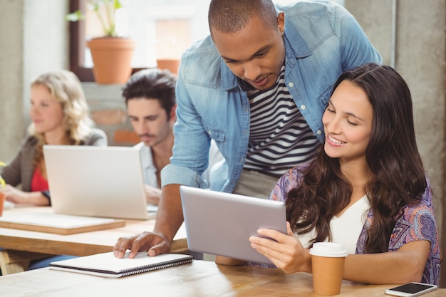 Smiling businesswoman showing digital tablet to male colleague in office