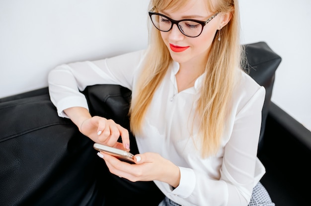 Smiling businesswoman using smartphone over gray background. Wearing in blue shirt and glasses.