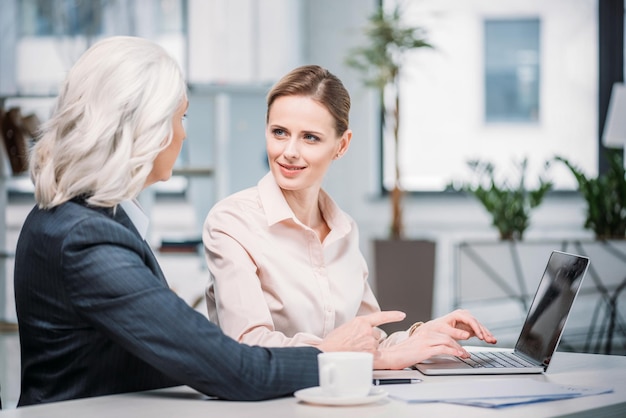 Smiling businesswomen talking while using laptop at workplace