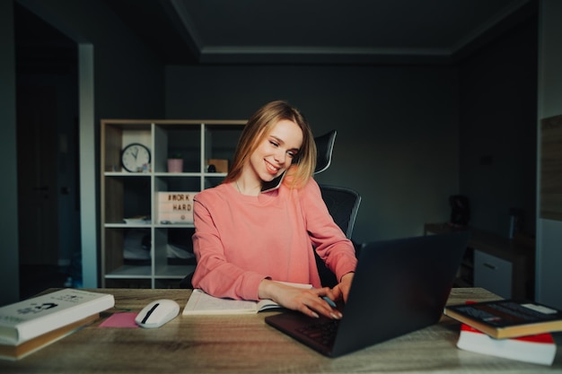 A smiling busy woman works remotely at home uses a laptop and talks on the phone with a happy face