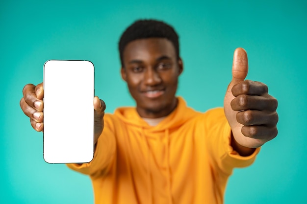 Smiling casual black man pointing at blank white cell phone screen in studio