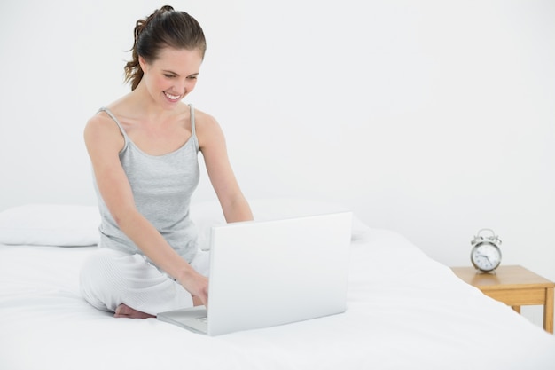 Smiling casual woman using laptop in bed